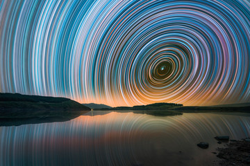 Wall Mural - Beautiful night landscape with small lake and mountains. The colorful star trails on the sky. Night time lapse photography..