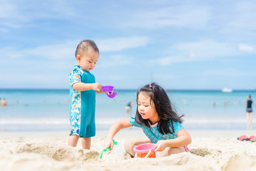 4 years old Little asian girl playing on the beach with her 1 year old baby brother.Children in nature with beautiful sea, sand and blue sky.Happy kids on vacations at seaside Sibling on Vacation.