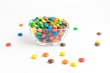 Group Of Small Mixed Colored Chocolate Coated Candies In A Transparent Glass Bowl On A Table, Isolated On White Background, Side View Photo Of Yellow, Orange, Green, Red And Brown Sweets