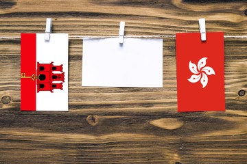 Hanging flags of Gibraltar and Hong Kong attached to rope with clothes pins with copy space on white note paper on wooden background.Diplomatic relations between countries.