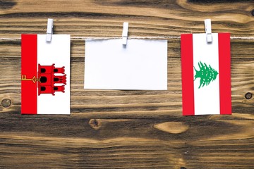 Hanging flags of Gibraltar and Lebanon attached to rope with clothes pins with copy space on white note paper on wooden background.Diplomatic relations between countries.