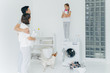 © VK Studio - Happy family do washing together in laundry room. Father and mother cuddle while look at daughter on top of washer, surrounded with basin of clothes to wash, pet and closet with folded linen