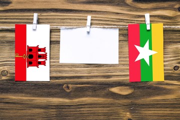 Hanging flags of Gibraltar and Myanmar attached to rope with clothes pins with copy space on white note paper on wooden background.Diplomatic relations between countries.