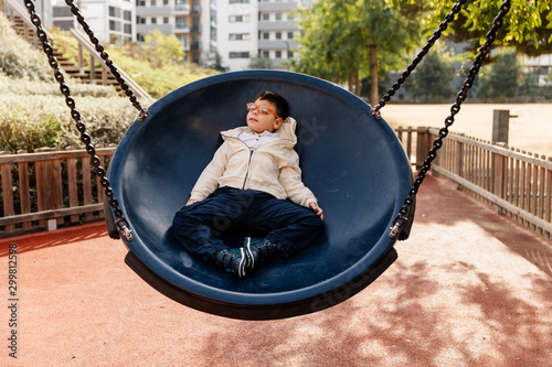 niño en el parque en columpio grande redondo balanceándose y riendo . Niño con pluri discapacidad. - Buy this stock photo and explore similar images at Adobe Stock | Adobe Stock