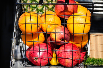 Orange, red apples and pomegranate fruits in a metallic basket displayed for sale at a street food market in Bucharest, Romania, side view of healthy fruits photograph with soft focus