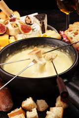 Gourmet Swiss fondue dinner on a winter evening with assorted cheeses on a board alongside a heated pot of cheese fondue with two forks dipping