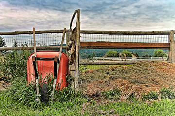 Wall Mural - A red wheelbarrow leans on a wooden, farm fence