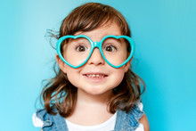 Portrait Of Cute Little Girl With Heart Shaped Glasses On Blue Background