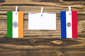 Hanging flags of India and Paraguay attached to rope with clothes pins with copy space on white note paper on wooden background.Diplomatic relations between countries.