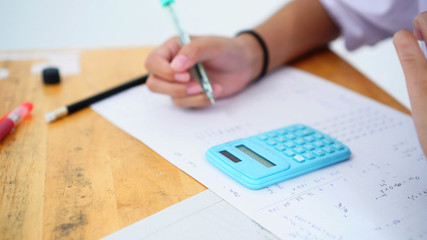 Evaluation or measurement concept. Student using calculator for used making mathematical calculations in exercise taking exam at school or university, taking in assessment paper on education study.