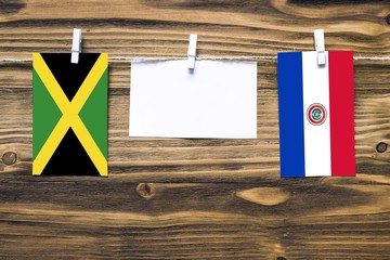 Hanging flags of Jamaica and Paraguay attached to rope with clothes pins with copy space on white note paper on wooden background.Diplomatic relations between countries.