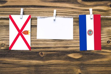 Hanging flags of Jersey and Paraguay attached to rope with clothes pins with copy space on white note paper on wooden background.Diplomatic relations between countries.