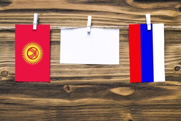 Wall Mural - Hanging flags of Kyrgyzstan and Russia attached to rope with clothes pins with copy space on white note paper on wooden background.Diplomatic relations between countries.