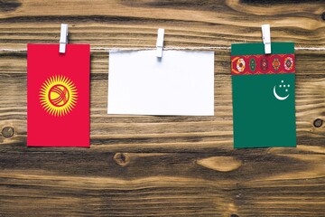 Hanging flags of Kyrgyzstan and Turkmenistan attached to rope with clothes pins with copy space on white note paper on wooden background.Diplomatic relations between countries.