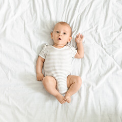 Funny newborn baby in bodysuit lying on bed at home