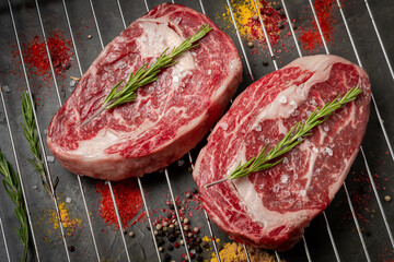 Wall Mural - Two juicy raw rib eye steaks prepared for grilling with spices and herbs.