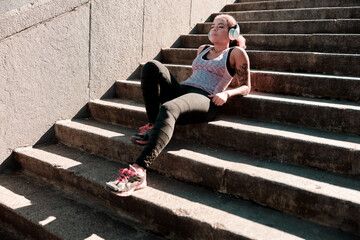 Relaxed Afro American lady in headphones resting on stairs outdoors