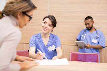 Poster - Clinician in uniform smiling at patient while pointing at medical document