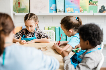 Poster - Group of diligent schoolkids sitting by table and making halloween decorations