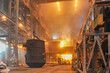 Crane lifting up filled metal container scrap in the burning ladle furnace with hot steel inside. Metallurgical factory