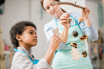 Poster - Cute boy looking at one of handmade Christmas decorations hanging on stick