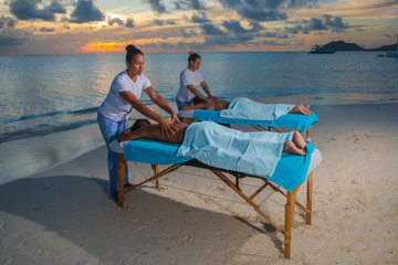 Women giving massage therapy stretch head neck outdoor at Caribbean beach to a couple on the massage table portable to relax. Caribbean turquoise water and sunset beach background .