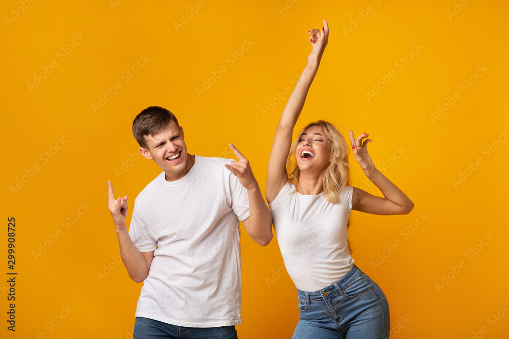 Carefree young couple dancing on yellow studio background - obrazy, fototapety, plakaty 