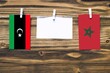 Hanging flags of Libya and Morocco attached to rope with clothes pins with copy space on white note paper on wooden background.Diplomatic relations between countries.