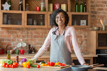 black woman cooking healthy salad at kitchen, smiling at camera