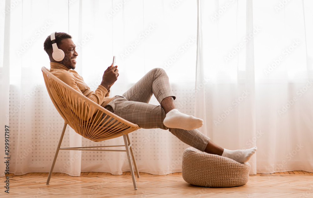 Man In Earphones Using Cellphone Sitting On Chair At Home - obrazy, fototapety, plakaty 