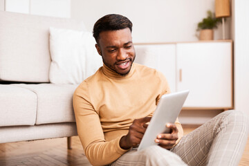 Poster - Afro Man Using Digital Tablet Sitting On Floor At Home