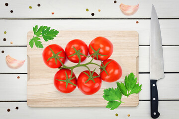 Top view of red fresh tomatoes with green leaves on a wooden board with aromatic spices.