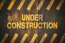 Under Construction Warning Sign With Yellow And Black Stripes Painted Over Cracked Wood