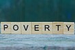 © butus - the word poverty from wooden letters on a gray table on a green background