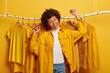 © wayhome.studio  - Carefree curly woman clothes buyer dances with happiness, raises arms, buys yellow clothing from new collection, rejoicing successful shopping day, being in high spirit, dances against outfits on rack