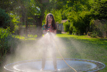 Girl Spraying  Garden With Hosepipe In Summer