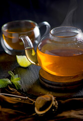 Poster - Hot tea in glass teapot and cup with steam on wood background