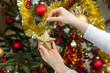 3. Kobieta ubiera choinkę na Boże Narodzenie. Dłoń kobiety trzyma złotą gwiazdę i zawiesza ozdobę na choinkę.