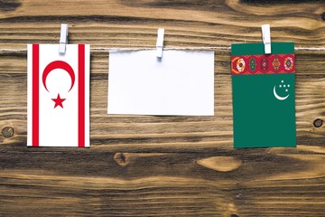 Hanging flags of Northern Cyprus and Turkmenistan attached to rope with clothes pins with copy space on white note paper on wooden background.Diplomatic relations between countries.