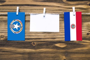 Hanging flags of Northern Mariana Islands and Paraguay attached to rope with clothes pins with copy space on white note paper on wooden background.Diplomatic relations between countries.