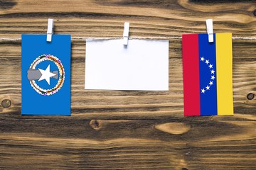 Hanging flags of Northern Mariana Islands and Venezuela attached to rope with clothes pins with copy space on white note paper on wooden background.Diplomatic relations between countries.