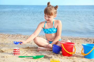 Wall Mural - Little girl playing with sand on sea beach