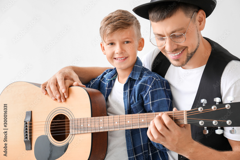 Man teaching his little son to play guitar on light background