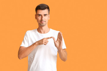 Wall Mural - Young deaf mute man using sign language on color background