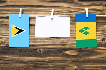 Hanging flags of Saint Lucia and Saint Vincent And The Grenadines attached to rope with clothes pins with copy space on white note paper on wooden background.Diplomatic relations between countries.