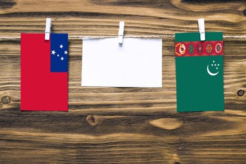Hanging flags of Samoa and Turkmenistan attached to rope with clothes pins with copy space on white note paper on wooden background.Diplomatic relations between countries.
