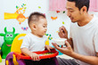 © sorapop - Father acting Mom feeding his son baby 1 year old on chair