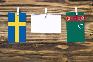 Hanging flags of Sweden and Turkmenistan attached to rope with clothes pins with copy space on white note paper on wooden background.Diplomatic relations between countries.