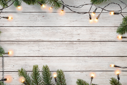 Fotografía Christmas lights bulb and pine leaves decoration on white wood plank, frame border design