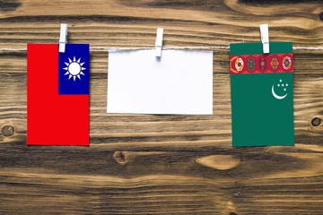 Hanging flags of Taiwan and Turkmenistan attached to rope with clothes pins with copy space on white note paper on wooden background.Diplomatic relations between countries.